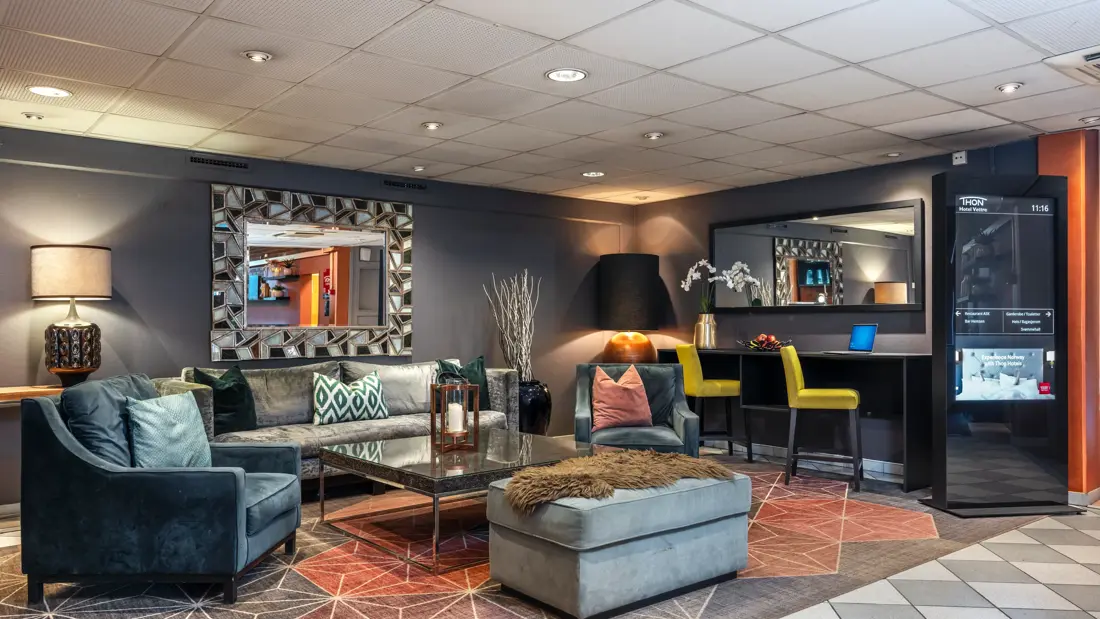 Sofa, lenestoler og puff i lobby med store speil på veggen.