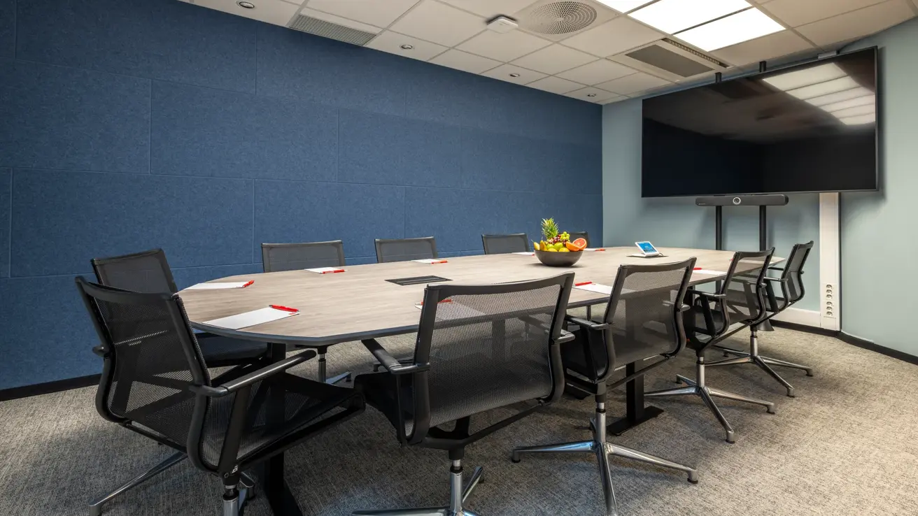 Møterom med styrebords oppsett til 10 personer, blå vegger, stor skjerm og fruktskål på bordet.