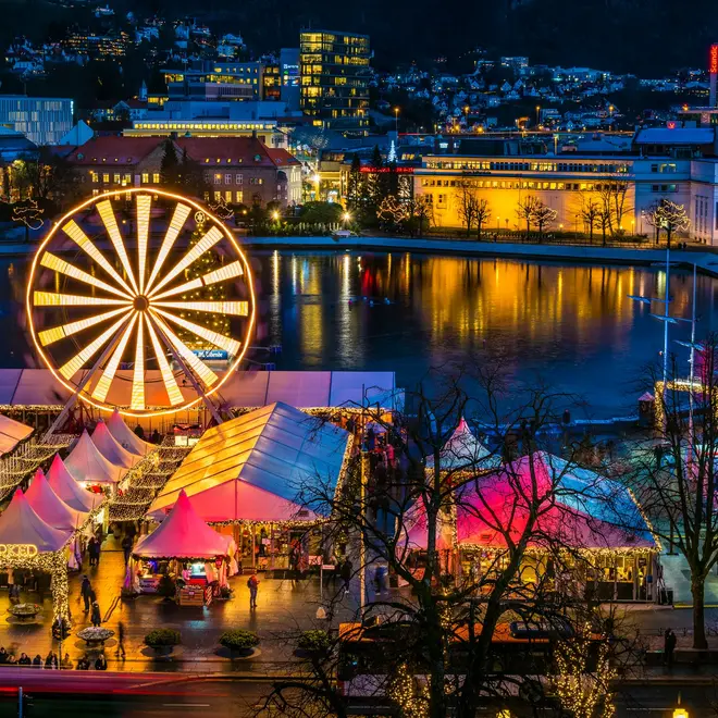 Julemarkedet i Bergen på Festplassen med opplyst pariserhjul og boder, speilet i Lille Lungegårdsvann en vinterkveld.