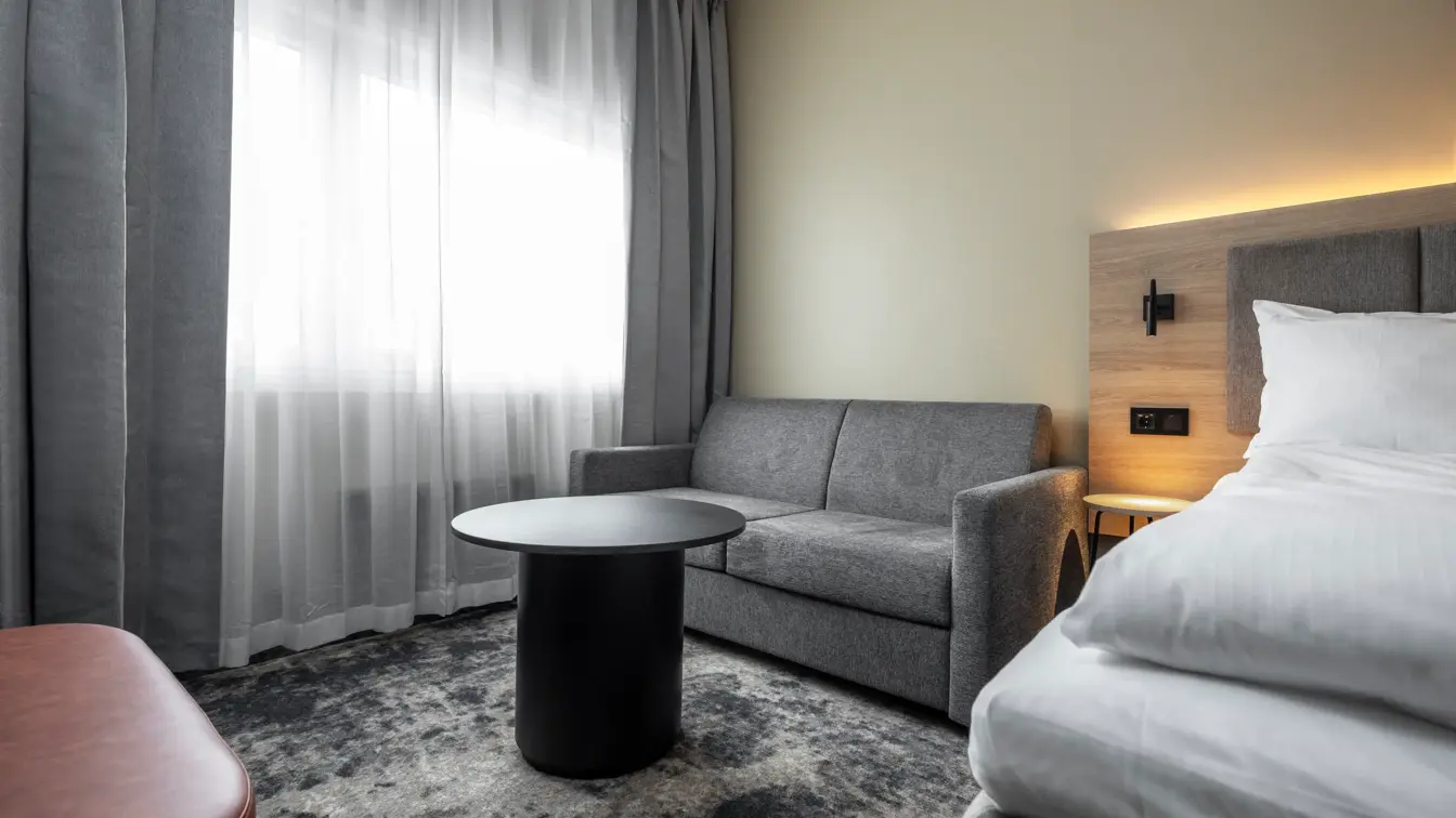 Dobbeltrom med dobbeltseng, sofa, bord, lange grå og hvite gardiner