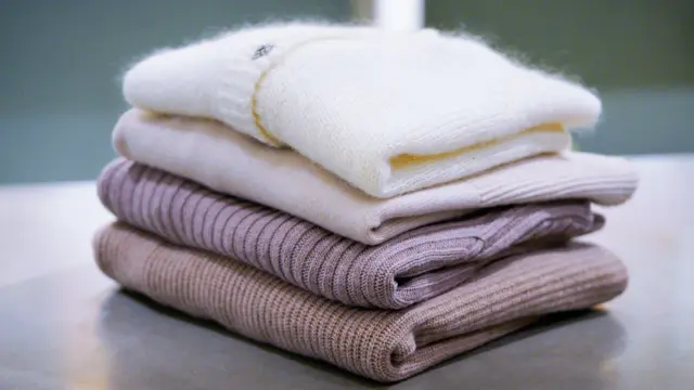 Stabel med ullgensere og cardigans liggende på ett bord 