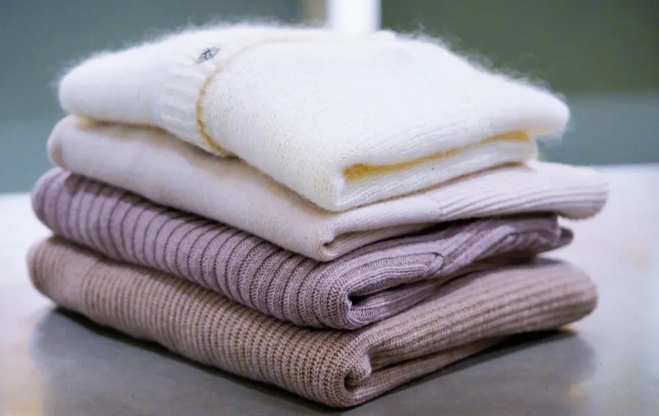 Stabel med ullgensere og cardigans liggende på ett bord 