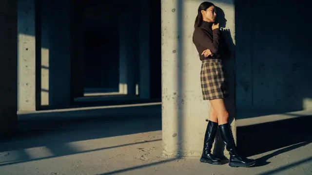 Jente med lange, svarte boots og tartanskjørt står inntil vegg