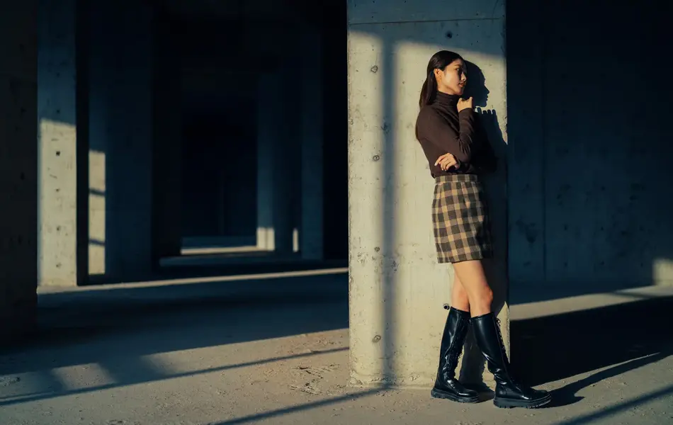 Jente med lange, svarte boots og tartanskjørt står inntil vegg