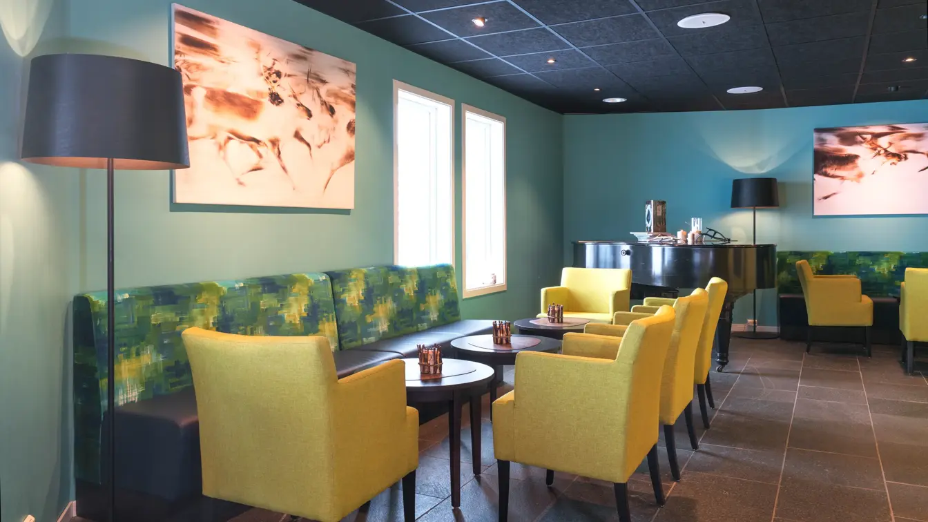 Fargerik lounge på Thon Hotel Kautokeino. Turkis vegg med stort bilde av reinsdyr. Stoler i gult og sofa i ulike grønne nyanser. 