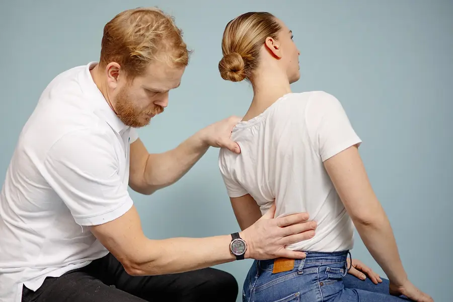 Mann kiropraktor som presser en dame i ryggen med hånden sin