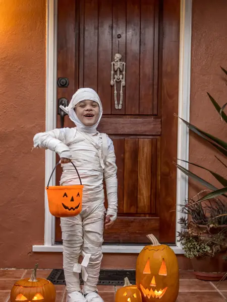 Happy 5 year old wearing a handmade mummy costume, trick or treating in a neighborhood