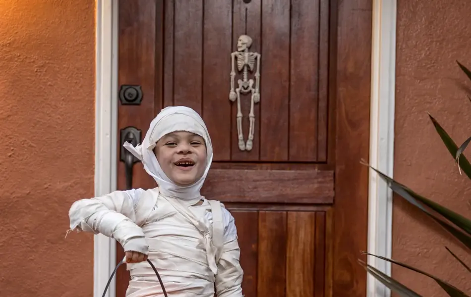Happy 5 year old wearing a handmade mummy costume, trick or treating in a neighborhood