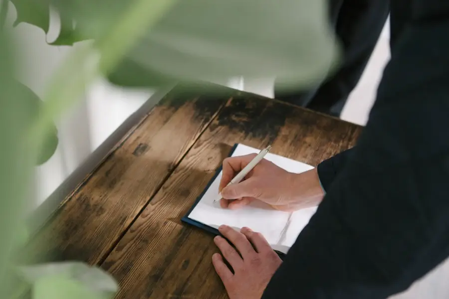 Hånd som signerer ark som ligger på trebord