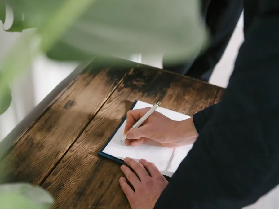 Hånd som signerer ark som ligger på trebord