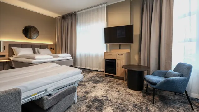 Junior suite med dobbeltseng og oppredd sovesofa, blå lenestol og sort bord, TV og TV benk under med minibar.