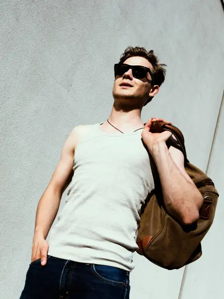 Mann med hvit singlett og skulderbag går ned trapp 