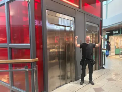 En smilende mann foran en heis i et kjøpesenter