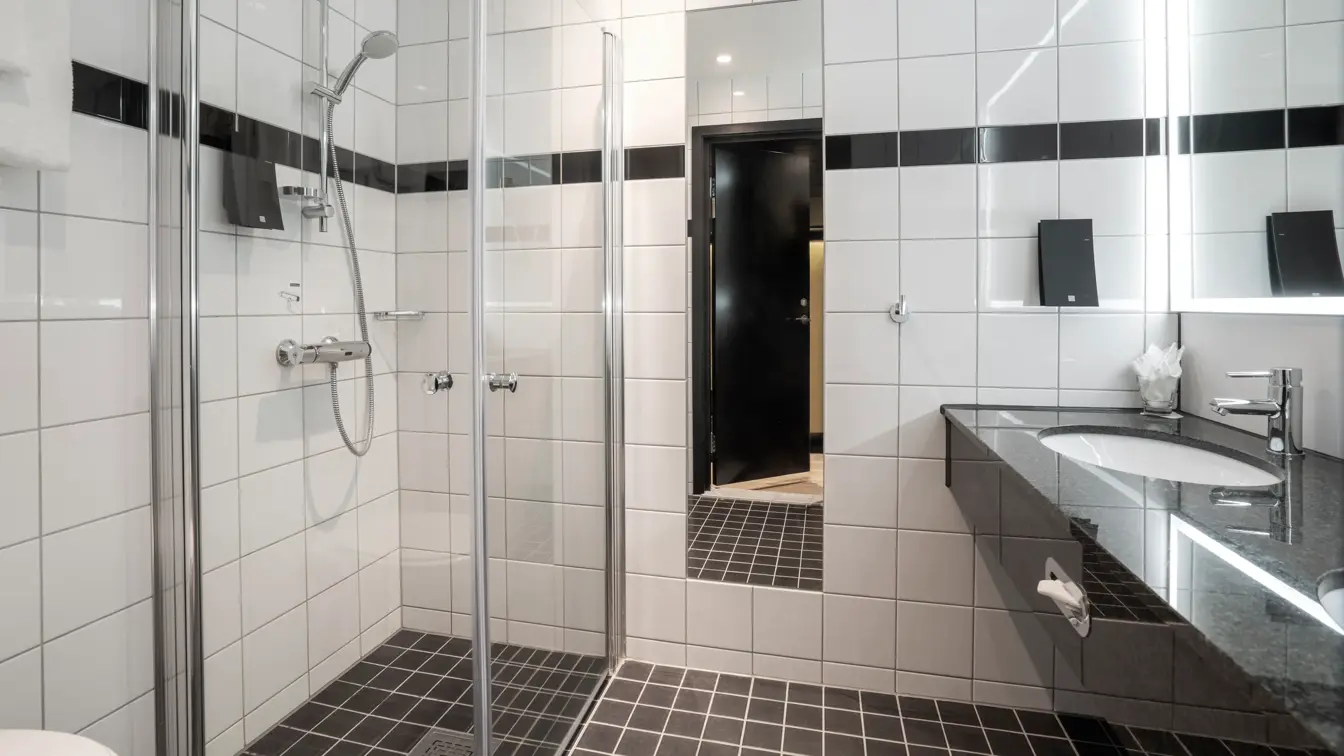 To vasker, speil, dusjkabinett, svarte gulvfliser, hvite veggfliser. 