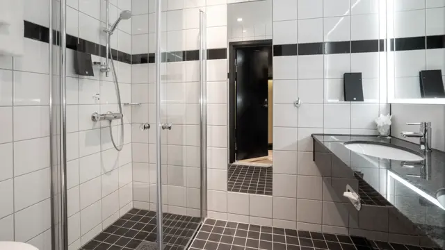 To vasker, speil, dusjkabinett, svarte gulvfliser, hvite veggfliser. 