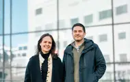Madelenè Jespersen og Georgios Skouroliakos poserer utendørs i vinterjakker foran en glassfasade