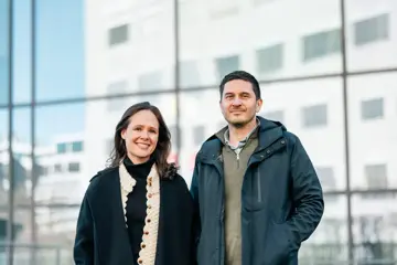 Madelenè Jespersen og Georgios Skouroliakos poserer utendørs i vinterjakker foran en glassfasade