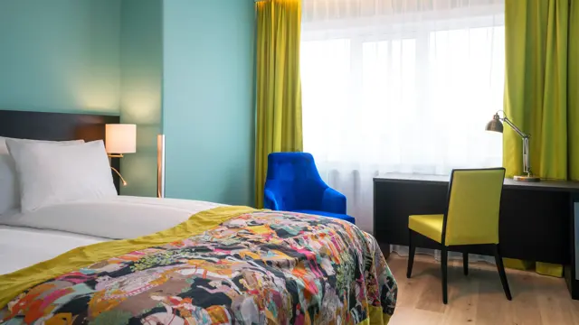 Twin room med hvit sengetøy, mønstret sengeteppe, gule gardiner, skrivepult og blå lenestol på Thon Hotel Europa i Oslo sentrum rett ved Slottsparken