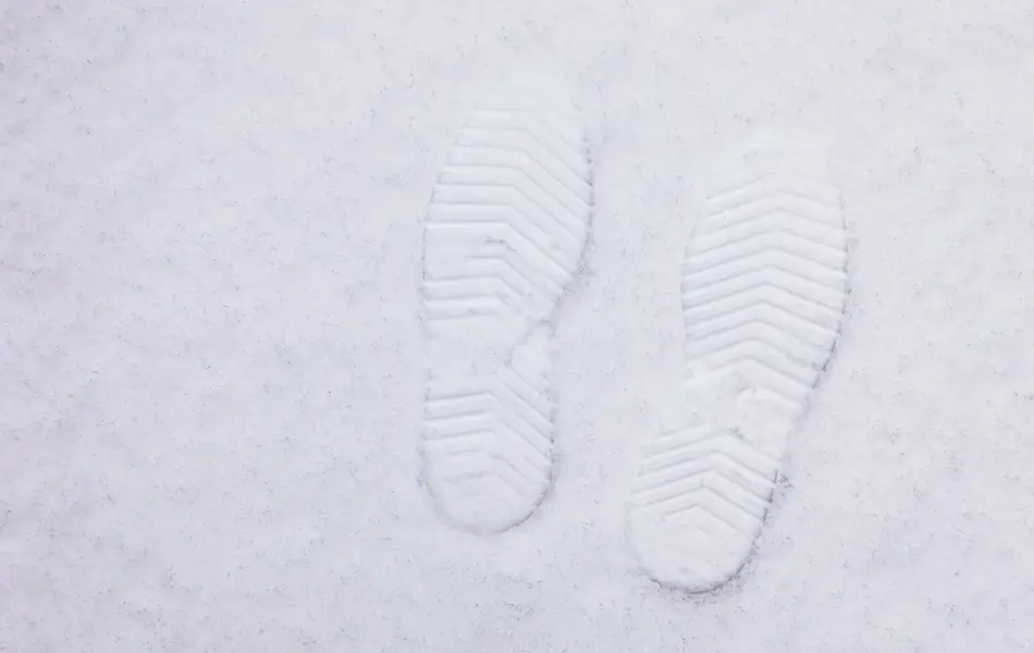 Et par svarte, fôrede vinterstøvler som står plassert i snøen.