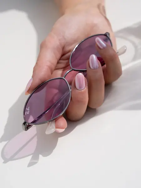 Hånd holder ovale smale solbriller med lilla glass.
