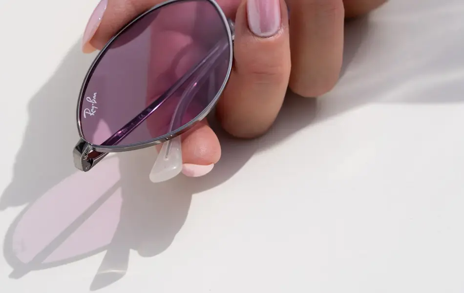 Hånd holder ovale smale solbriller med lilla glass.