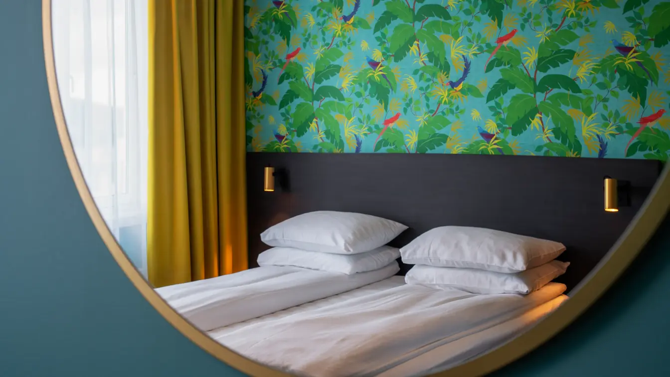 Rundt veggspeil, dobbeltseng, grønntapetvegg med mønster