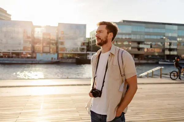 mann med hvit t-skjorte og åpen, lys beige linskjorte over og kamera rundt halsen