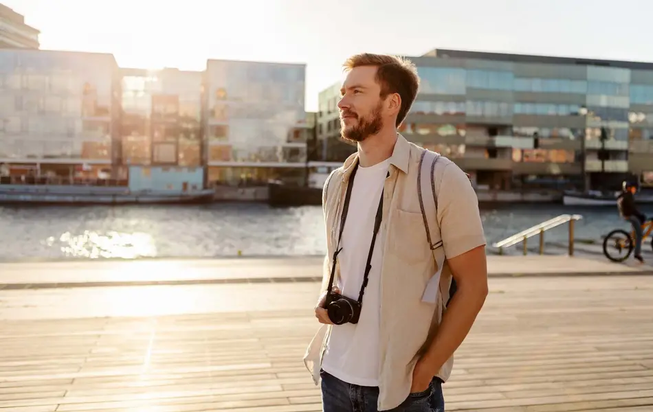mann med hvit t-skjorte og åpen, lys beige linskjorte over og kamera rundt halsen