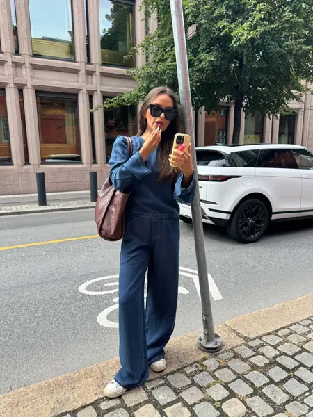 dame med jeans skjorte og bukse, brun veske, hun sminker seg