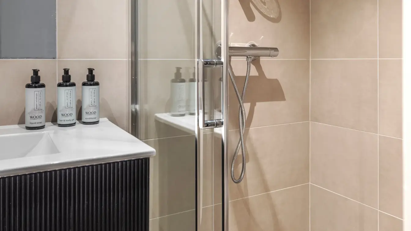 Flislagt bad med dusj, servant med såpedispensere på.