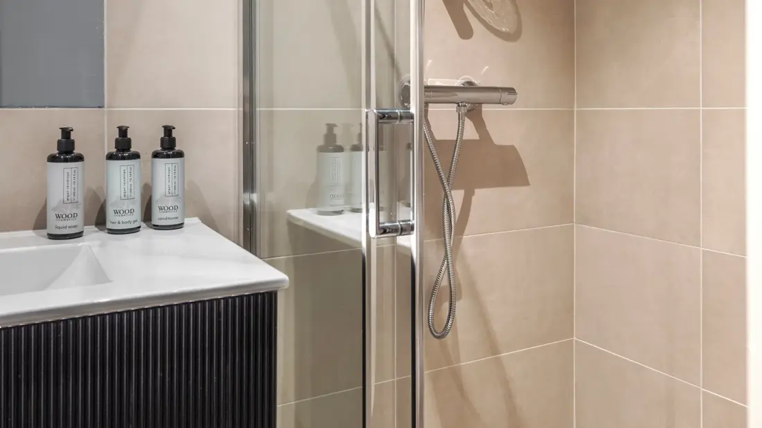 Flislagt bad med dusj, servant med såpedispensere på.