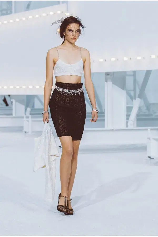 Dame som går på catwalken med hvit bh topp og sort skjørt med et tynt belte med glitter