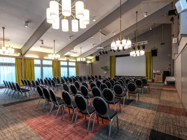 Stor sal med kino oppsett, lysekroner i taket, store vinduer med gule gardiner, stort lerret foran i lokalet