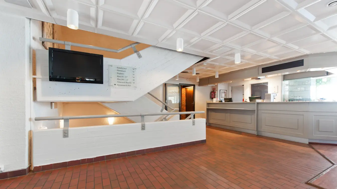 Lobby og resepsjonsområdet med mursteinsgulv, TV og trapper hos Thon Hotel Sandnes
