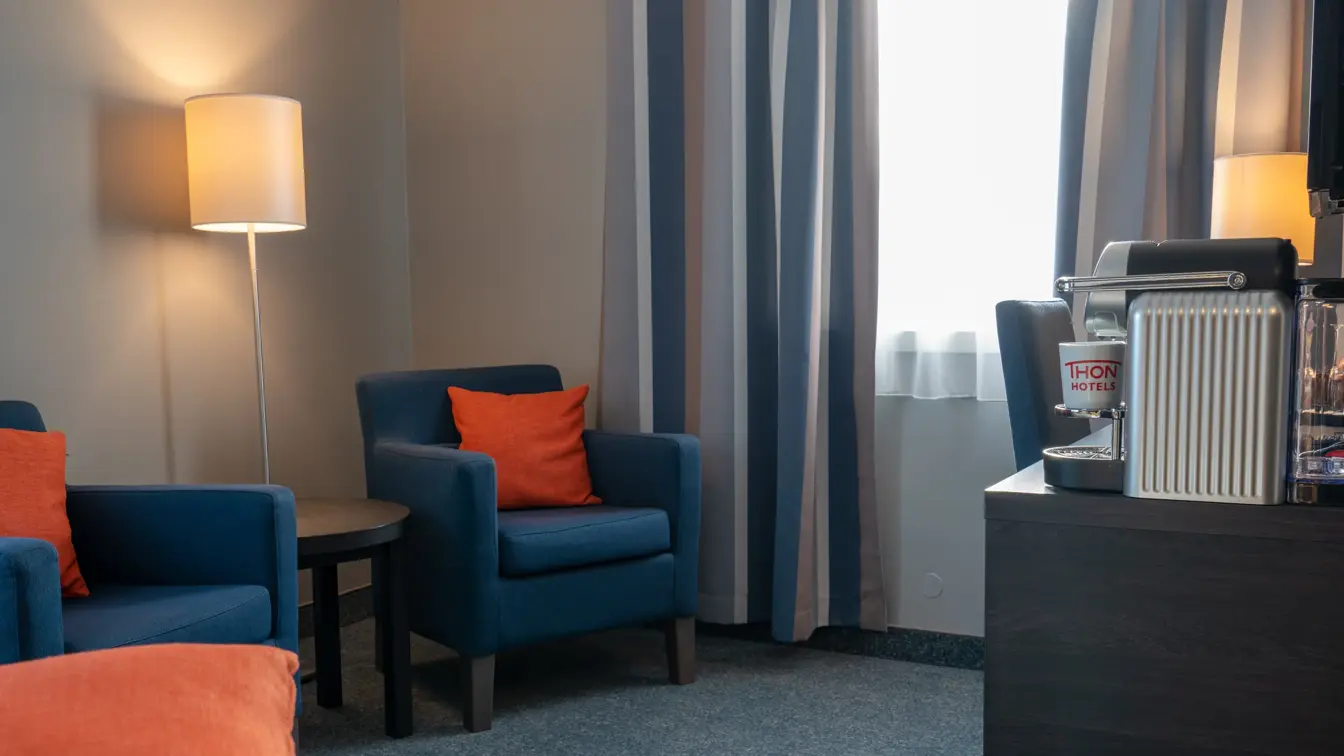 To blå lenestoler, salongbord, skrivebord, vindu, stol.