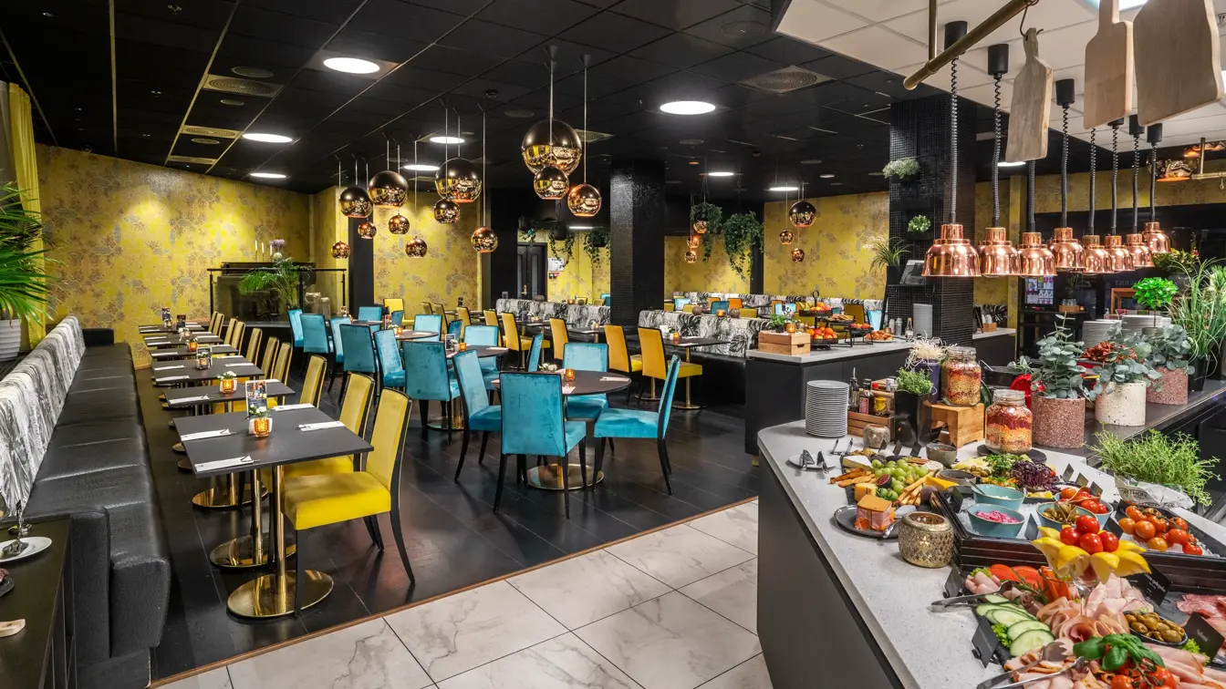 Frokostsal med frokostbuffet på høyre side. Gul tapet, gule og blå stoler.