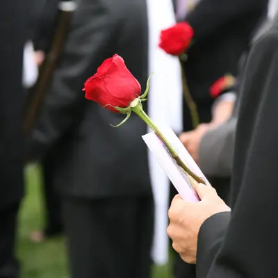 Person i sort dress holder en rød rose blant andre dresskledde mennesker i en begravelse