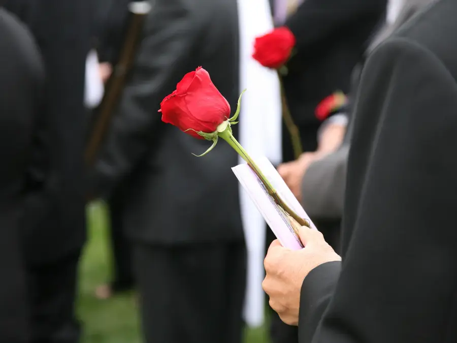 Person i sort dress holder en rød rose blant andre dresskledde mennesker i en begravelse