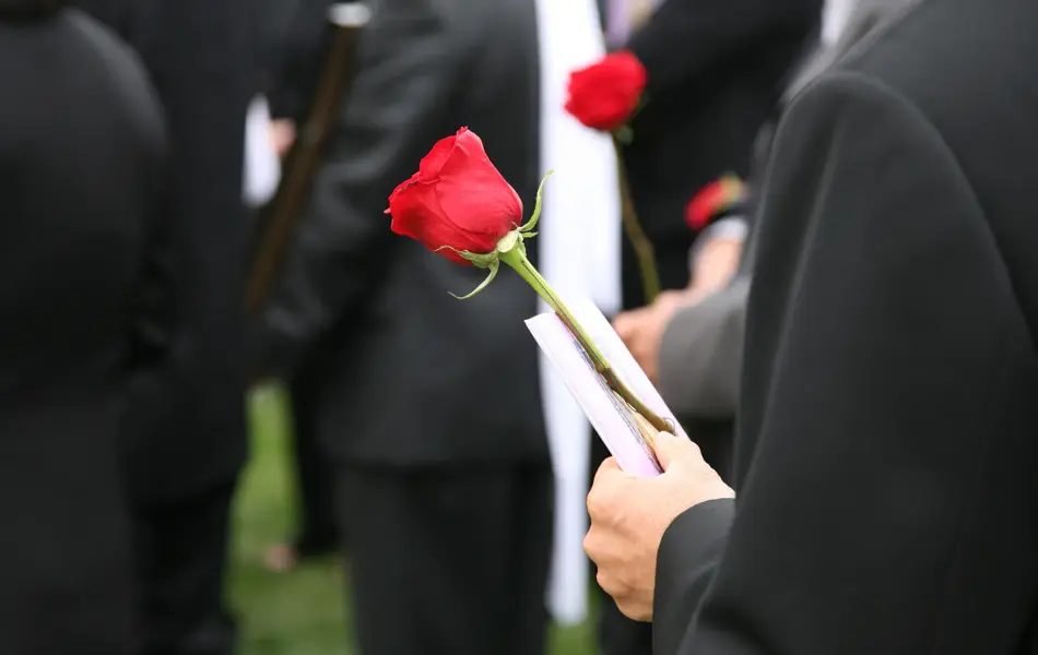 Person i sort dress holder en rød rose blant andre dresskledde mennesker i en begravelse