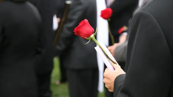Person i sort dress holder en rød rose blant andre dresskledde mennesker i en begravelse