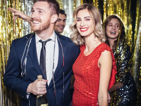 Mann med blå dress og dame med rød paljettkjole står i et festlokale som er pyntet med glitterremser