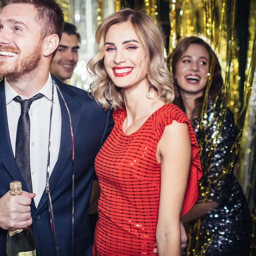 Mann med blå dress og dame med rød paljettkjole står i et festlokale som er pyntet med glitterremser