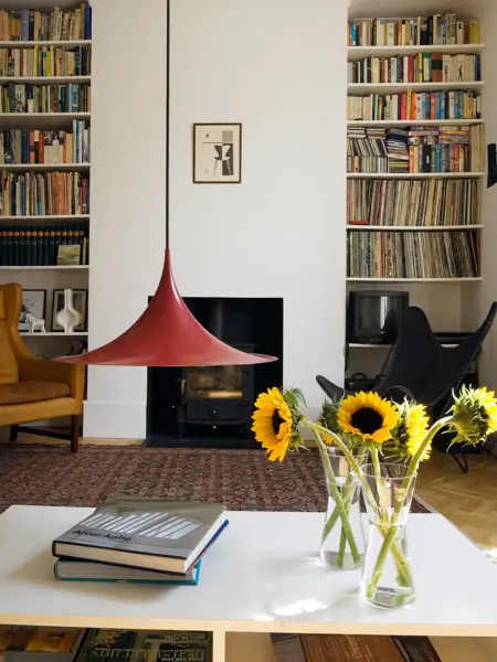 Stue med rød statementlampe, bord med gule solsikker og hyller med LP-plater og bøker i bakgrunnen 