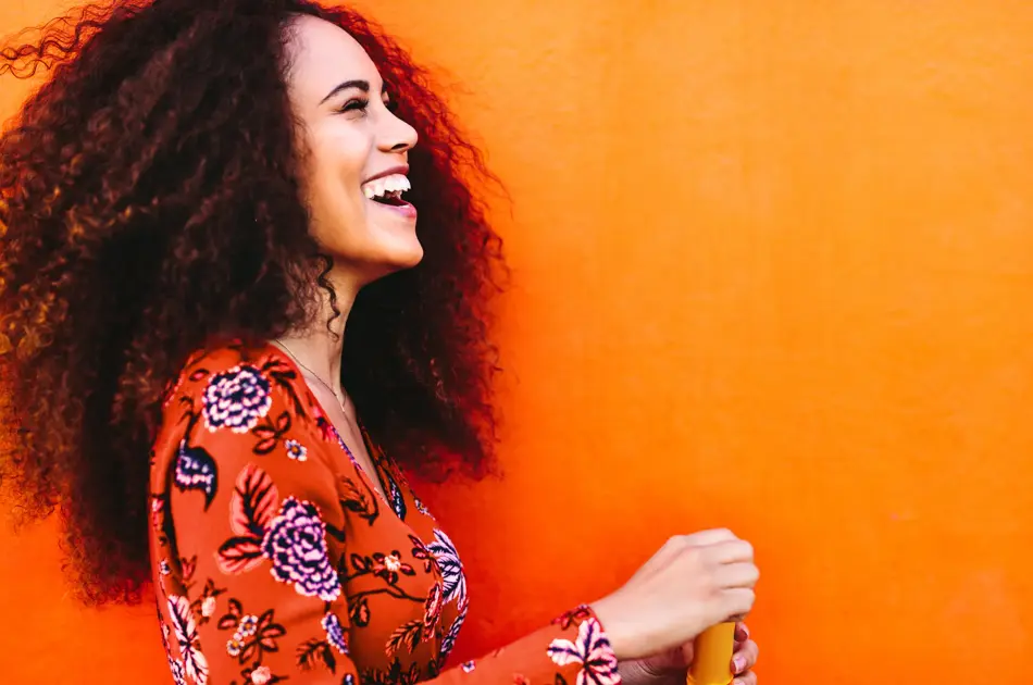 Side view shot of attractive female with soap bubbles. Young woman having fun against orange background.
