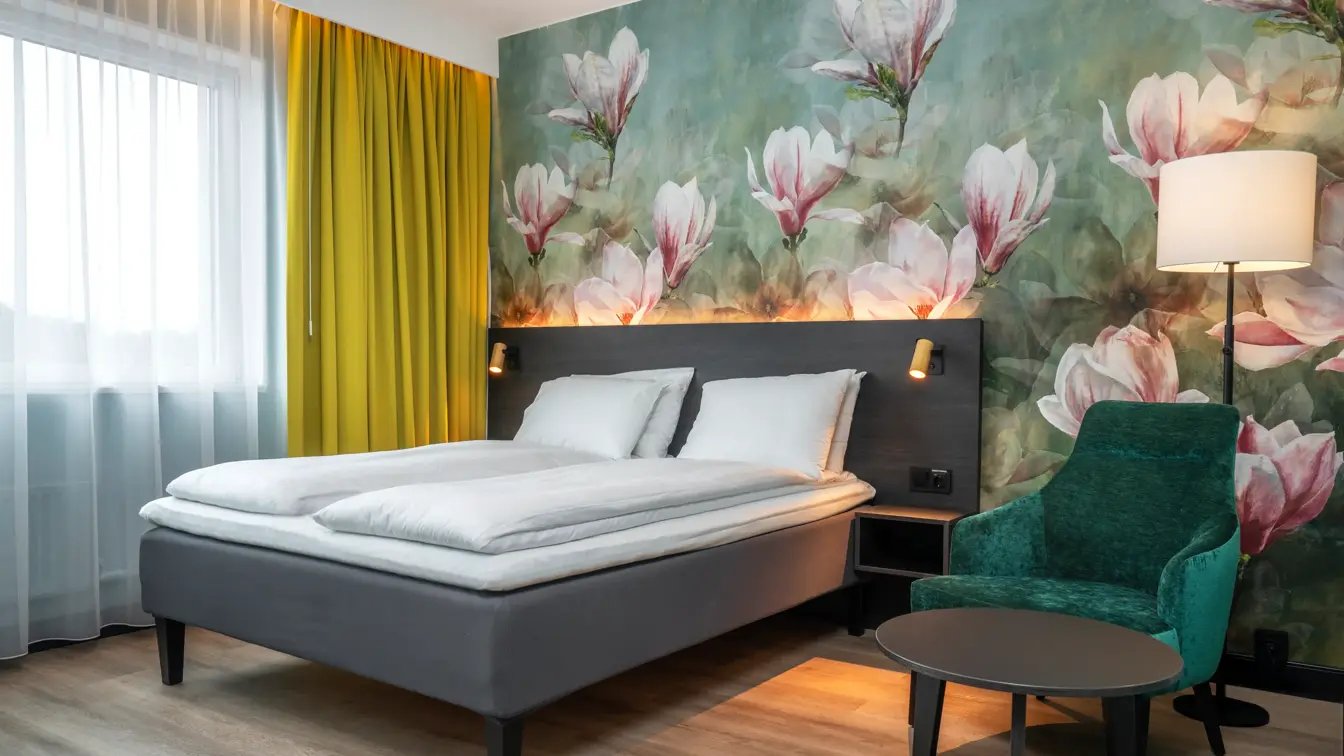 Blomstertapetvegg, dobbeltseng, grønn lenestol, gulvlampe, vindu, gule gardiner