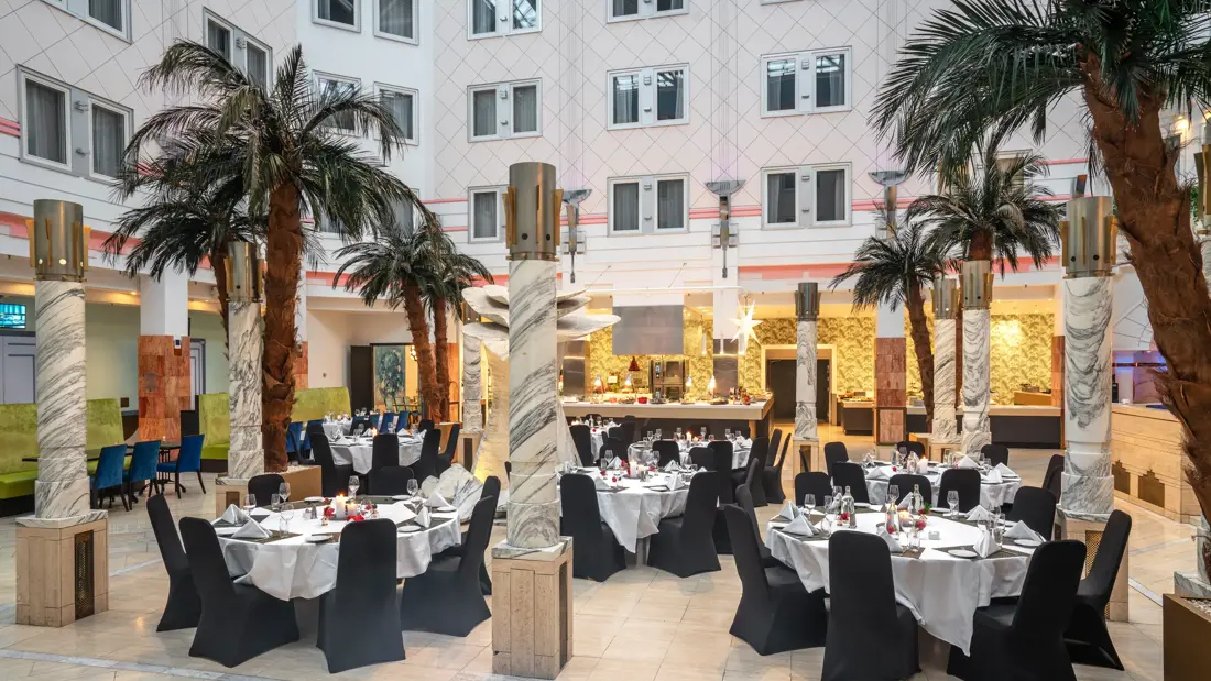 Runde oppdekede bord, palmer, åpent lokale, høyt under taket, svarte stoler