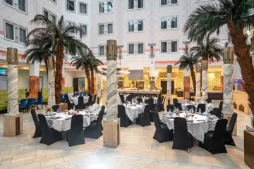 Runde oppdekede bord, palmer, åpent lokale, høyt under taket, svarte stoler