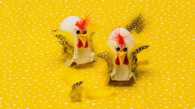 To høner, fylt med hvert sitt egg, laget av eggekartong, filtbiter og fjær på en gulprikkede bakgrunn