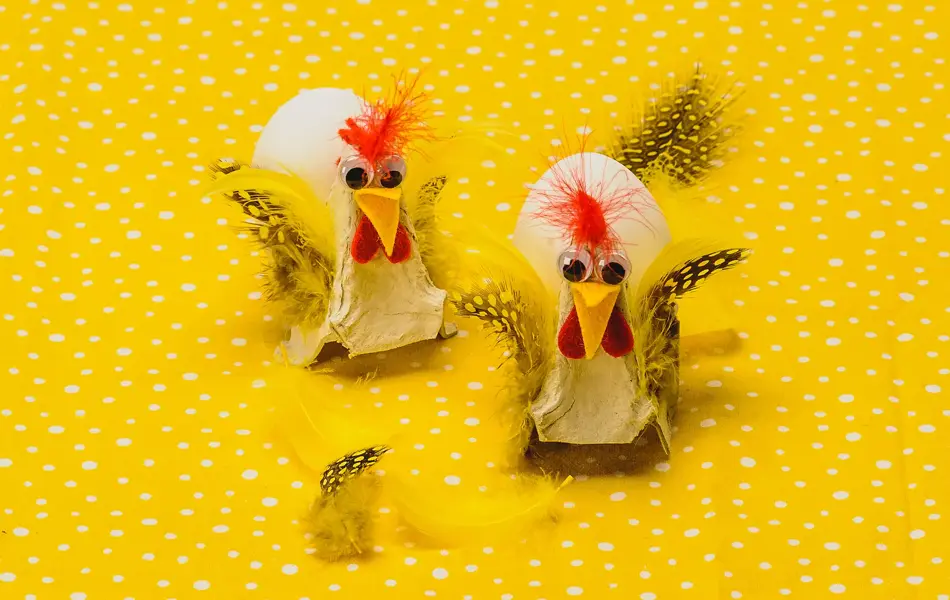 To høner, fylt med hvert sitt egg, laget av eggekartong, filtbiter og fjær på en gulprikkede bakgrunn