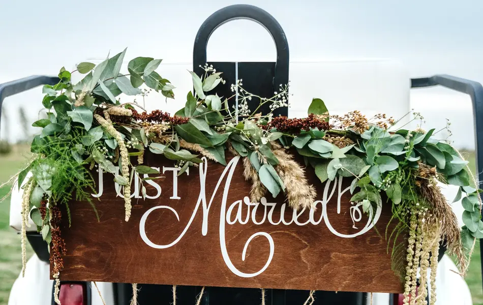 A Wedding Signboard just married, on a golf carriage adorned with flowers and tin cans on the golf course. Wedding ceremony and transportation.